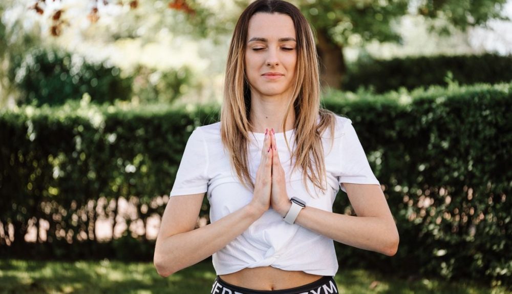 A serene moment of a woman practicing yoga with namaste pose outdoors, embracing mindfulness.