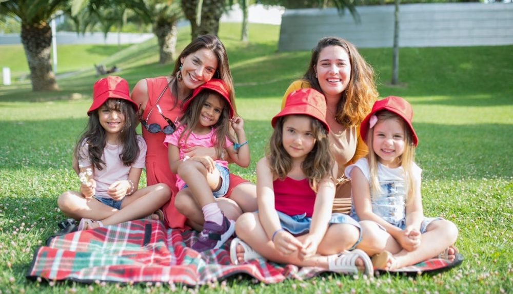 Friends enjoying a sunny day picnic on grass with bucket hats and smiles in a Portuguese park.